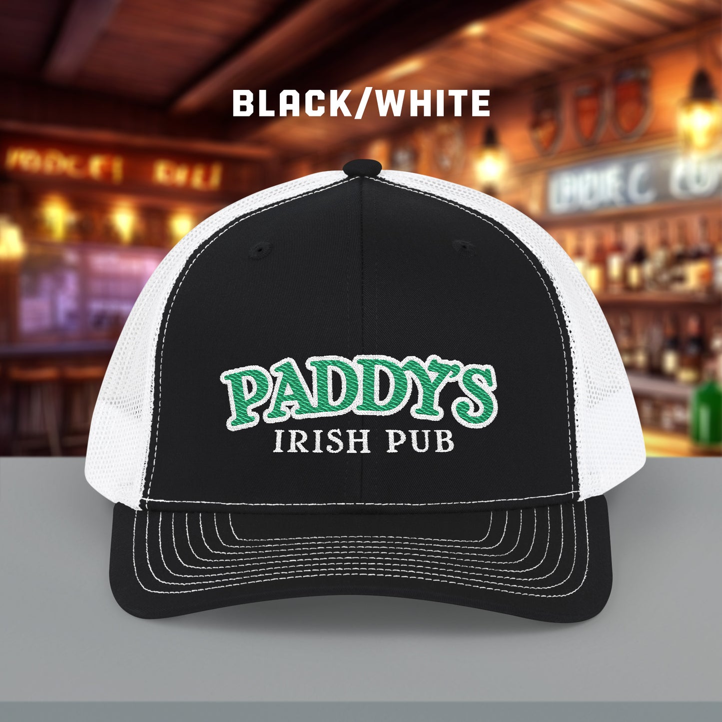 Black and white Richardson 112 trucker cap with green Paddy’s Irish Pub embroidered logo shown in a bar.