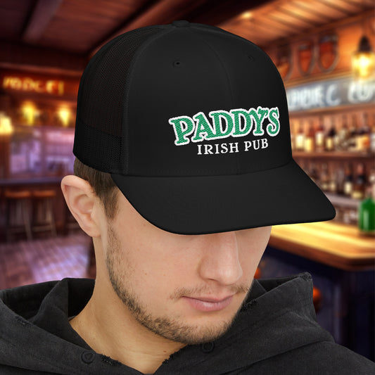 Man wearing all Black Richardson 112 trucker cap with green Paddy’s Irish Pub embroidered logo in a bar.