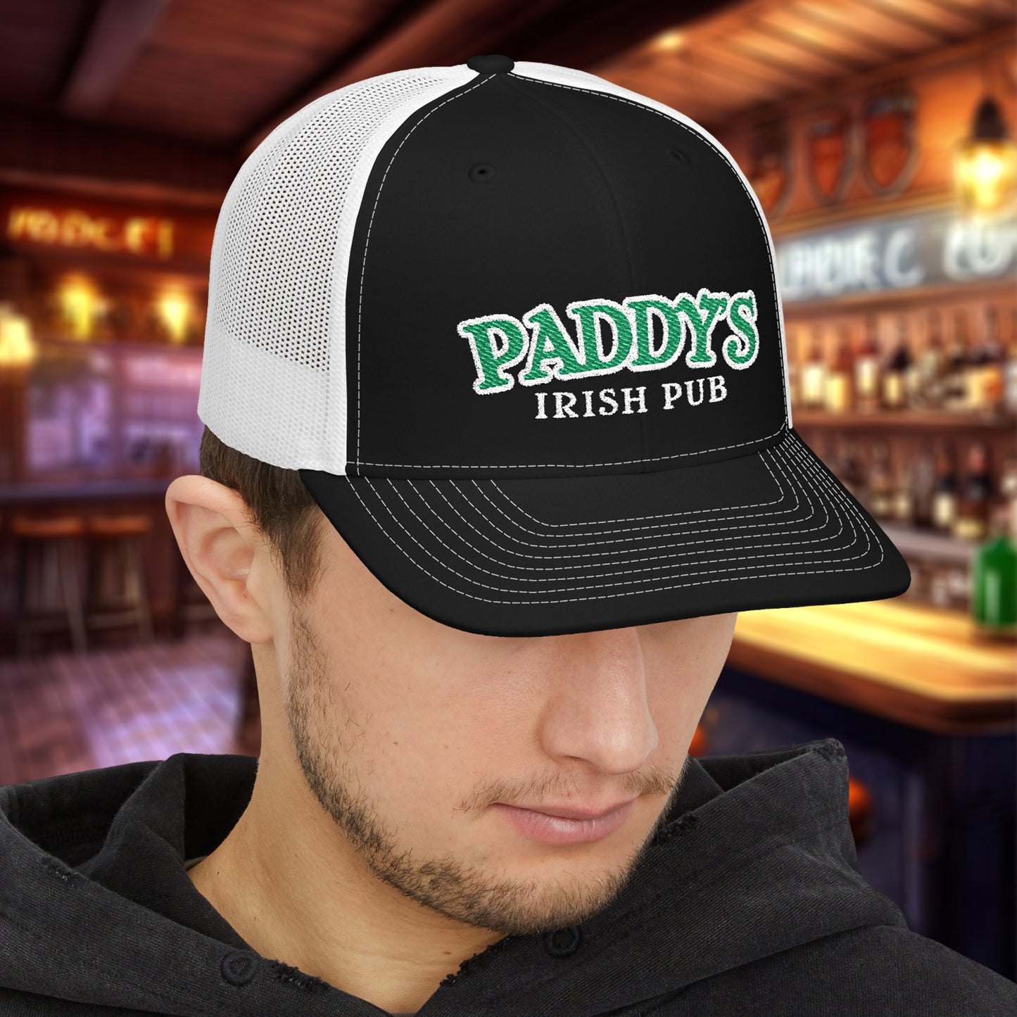 Man wearing Black and white Richardson 112 trucker cap with green Paddy’s Irish Pub embroidered logo in a bar.
