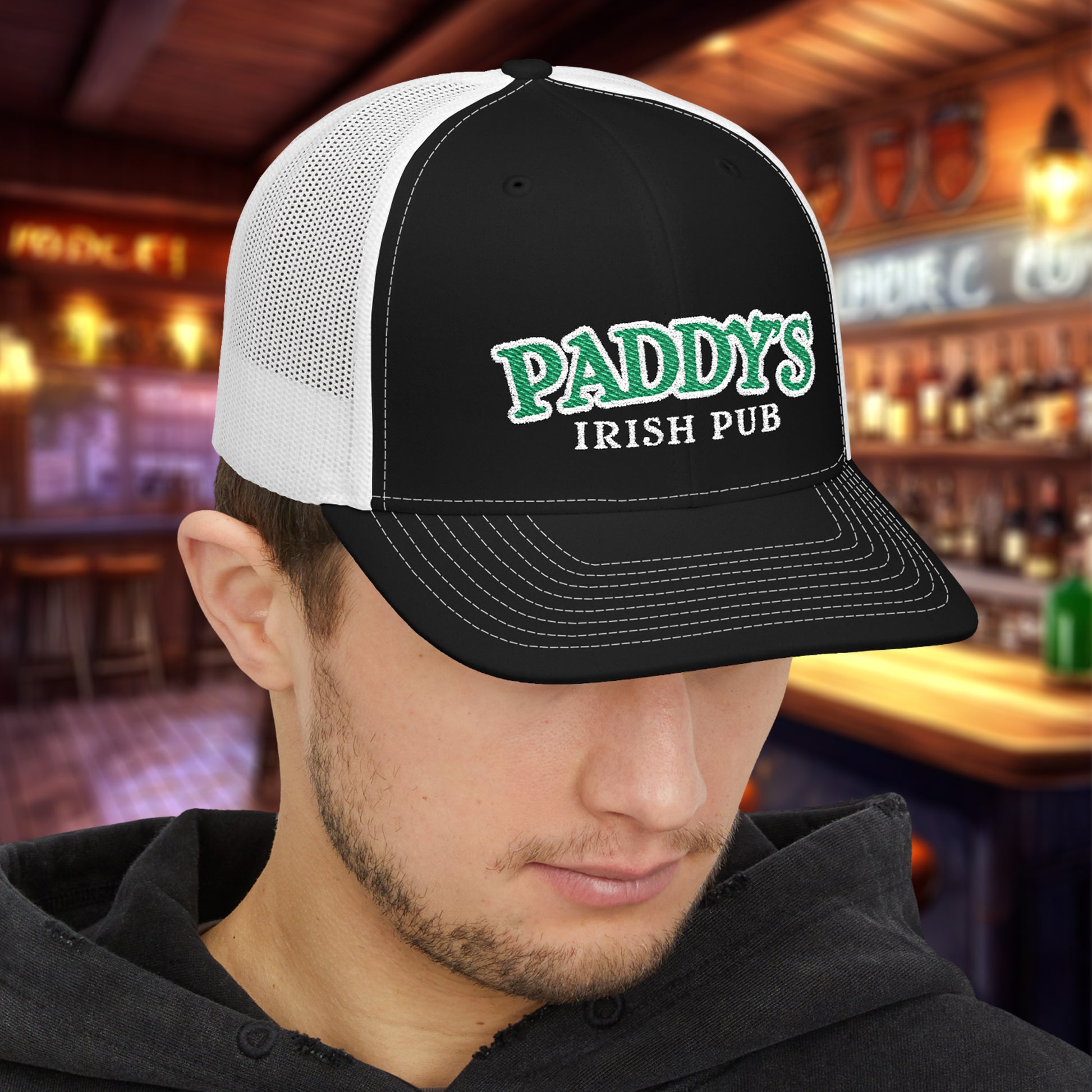 Man wearing Black and white Richardson 112 trucker cap with green Paddy’s Irish Pub embroidered logo in a bar.