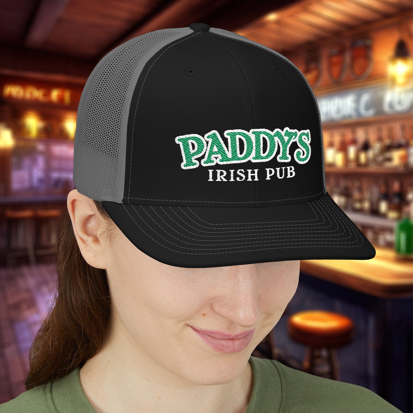 Woman wearing Black charcoal Richardson 112 trucker cap with green Paddy’s Irish Pub embroidered logo in a bar.