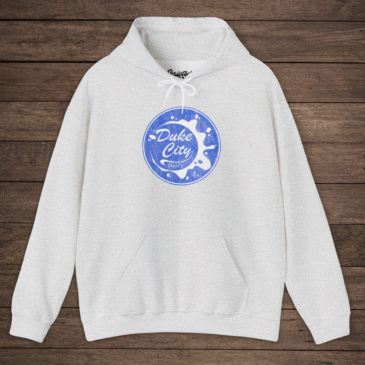Ash hoodie with 'Duke City Dairy' logo from Pluribus on a wooden background.
