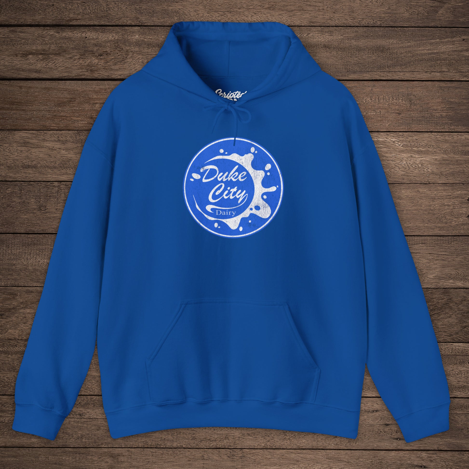 Royal blue hoodie with 'Duke City Dairy' logo from Pluribus on a wooden background.
