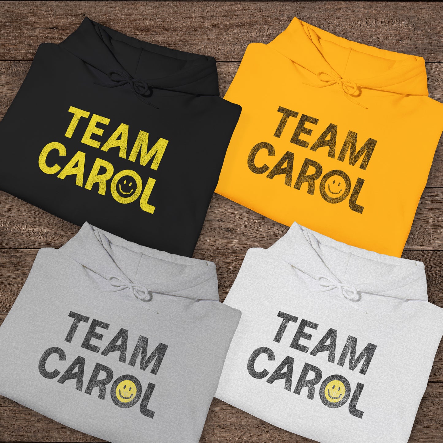 Four folded unisex Heavy Blend pullover hoodie sweatshirts with TEAM CAROL vintage distressed smiley graphic