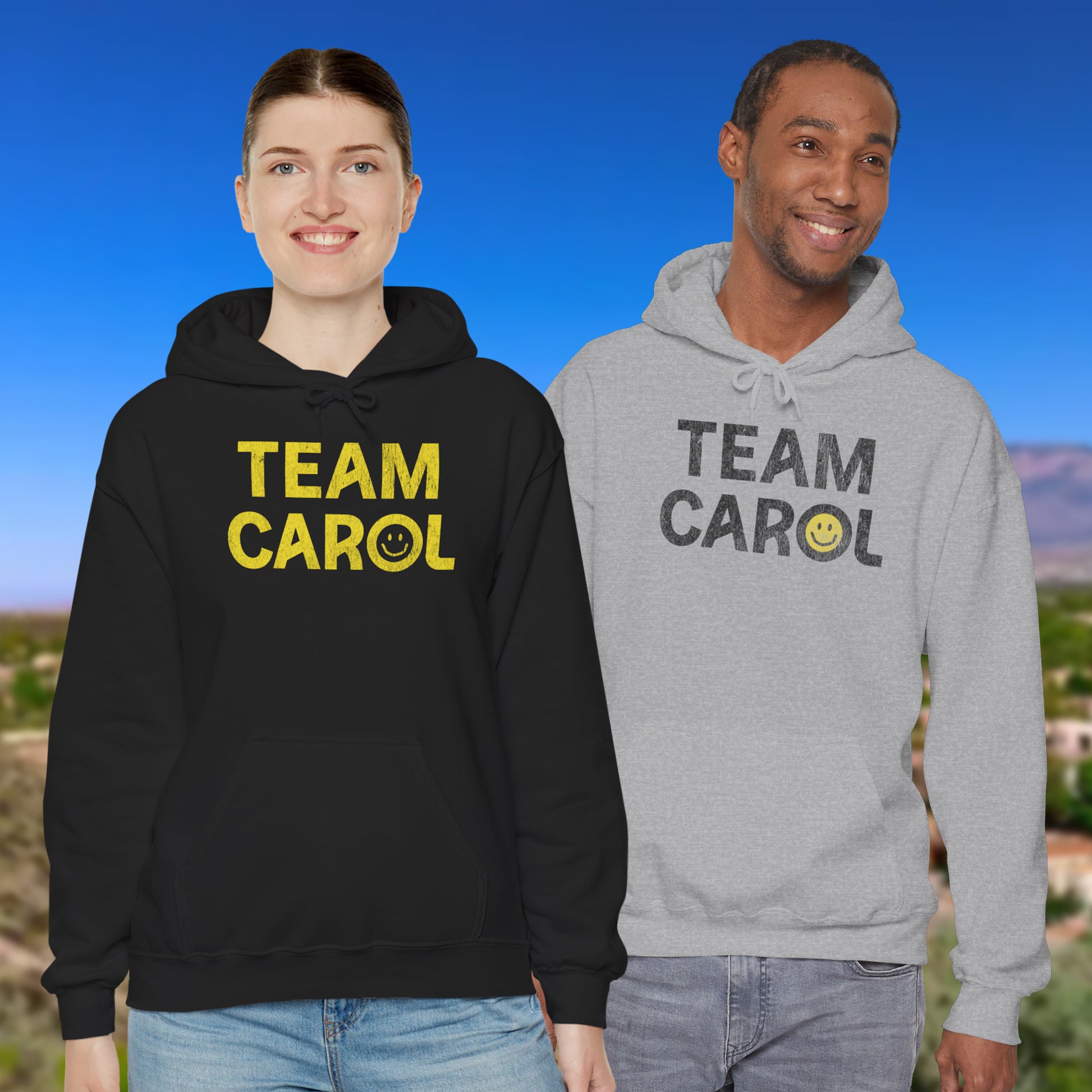 Two people wearing unisex Heavy Blend pullover hoodie sweatshirts with TEAM CAROL vintage distressed smiley graphic