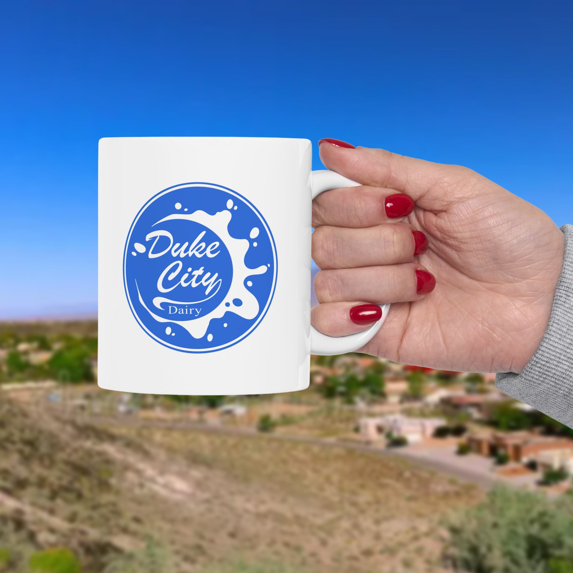 Hand holding a mug with 'Duke City Dairy' logo against a scenic background