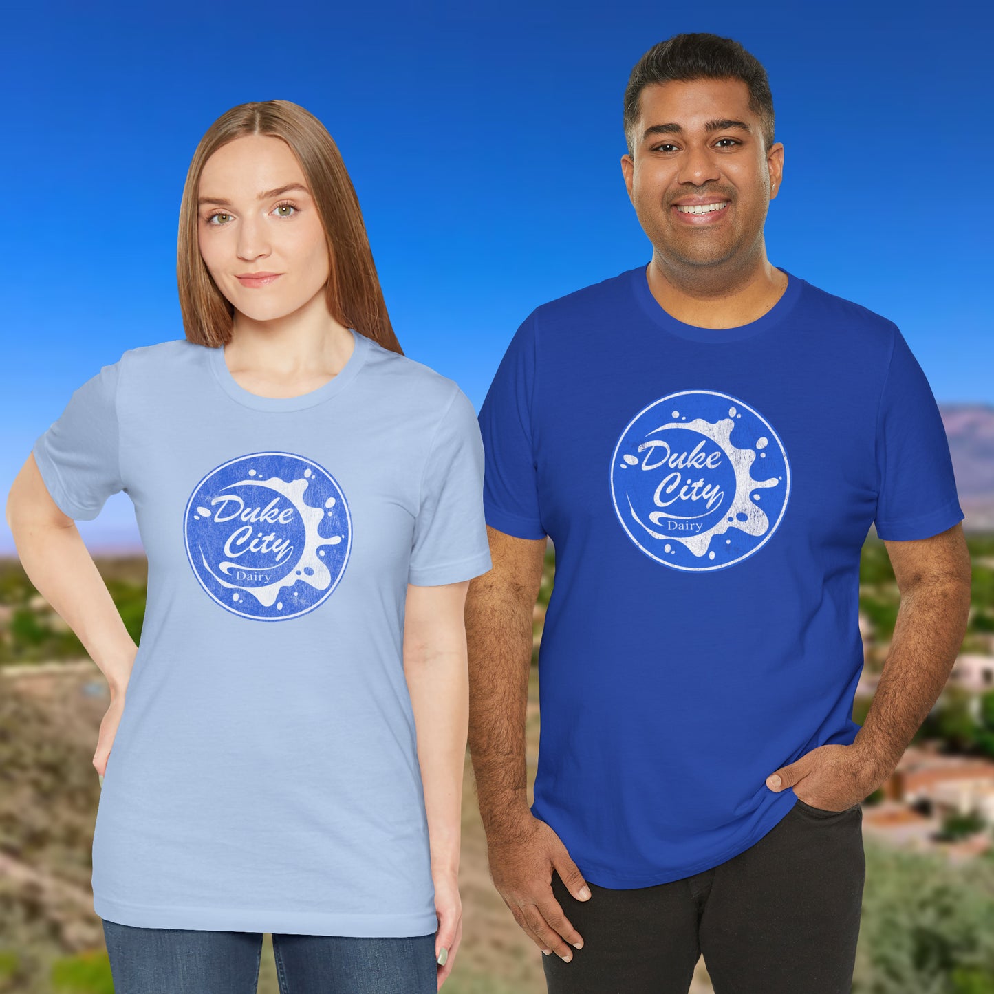 Two people wearing blue t-shirts with vintage distressed Duke City Dairy logo inspired by TV Show Pluribus.