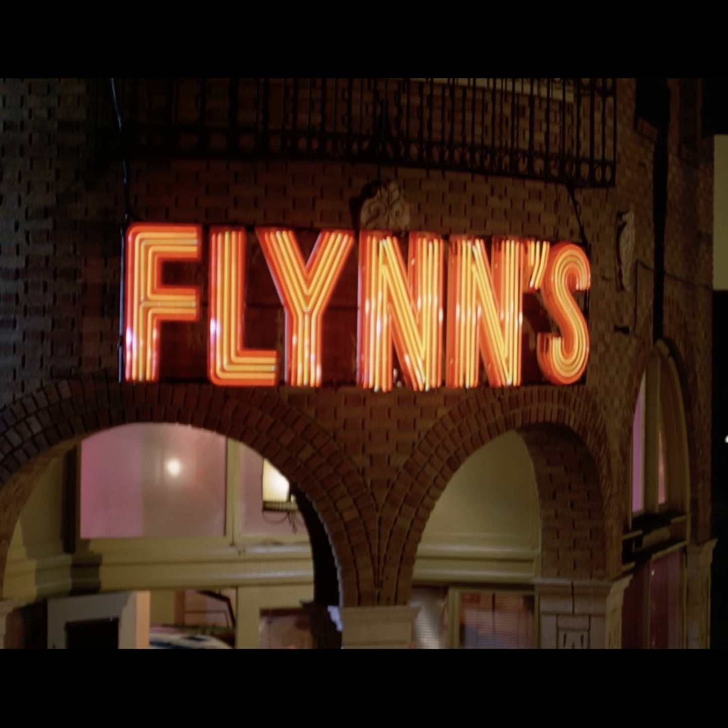 Scene from Tron - a neon sign reading 'FLYNN'S' arcade in a brick archway.
