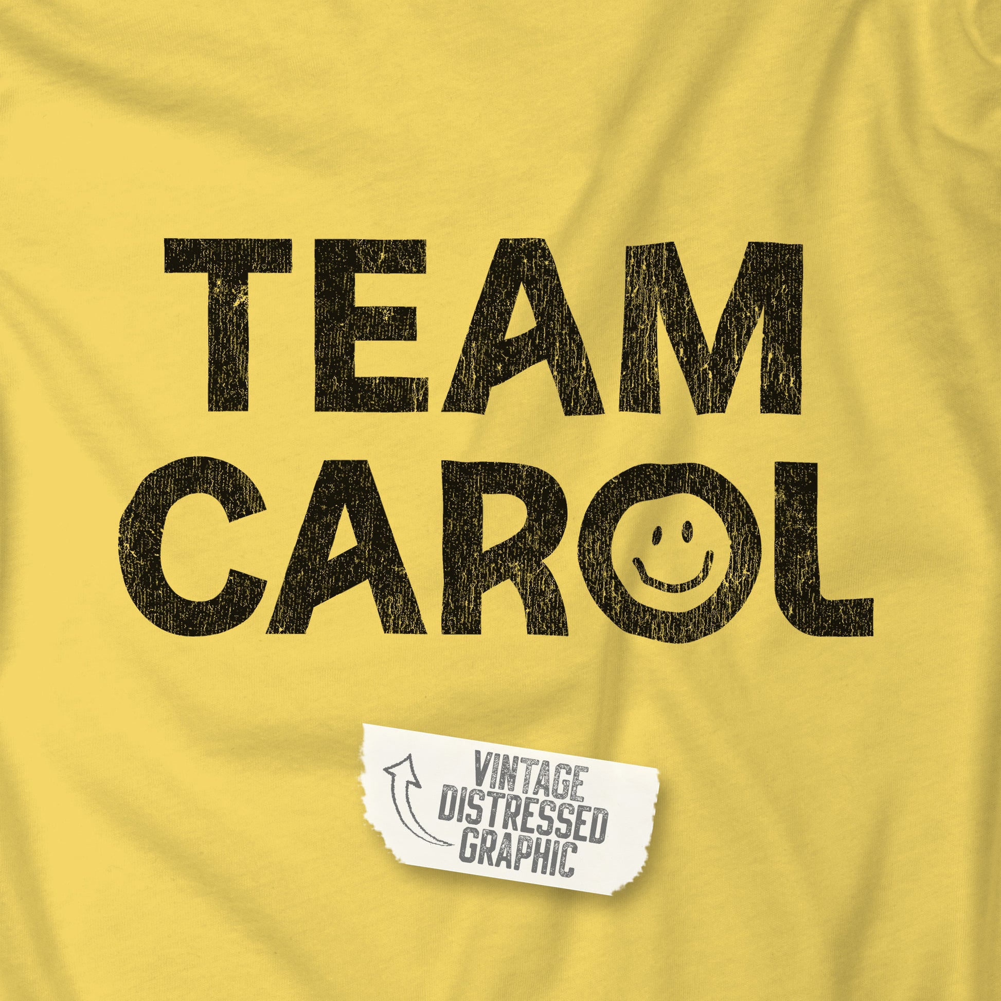 Closeup of yellow TEAM CAROL t-shirt inspired by Pluribus with vintage distressed smiley face graphic in black