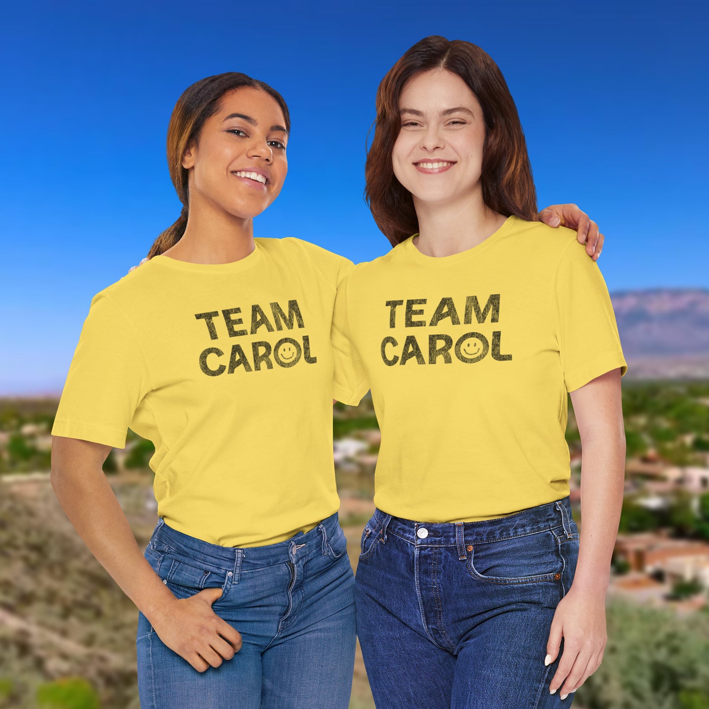 Two people wearing yellow 'Team Carol' shirts with a scenic background.