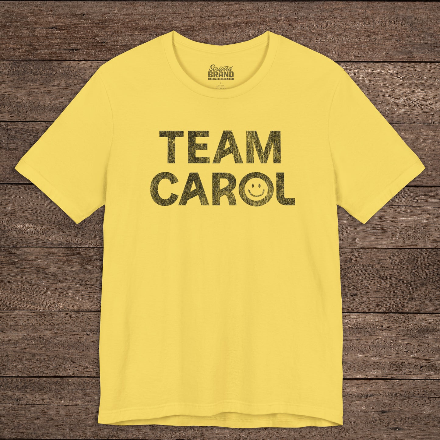 Front view of yellow TEAM CAROL t-shirt inspired by Pluribus with vintage distressed smiley face graphic in black
