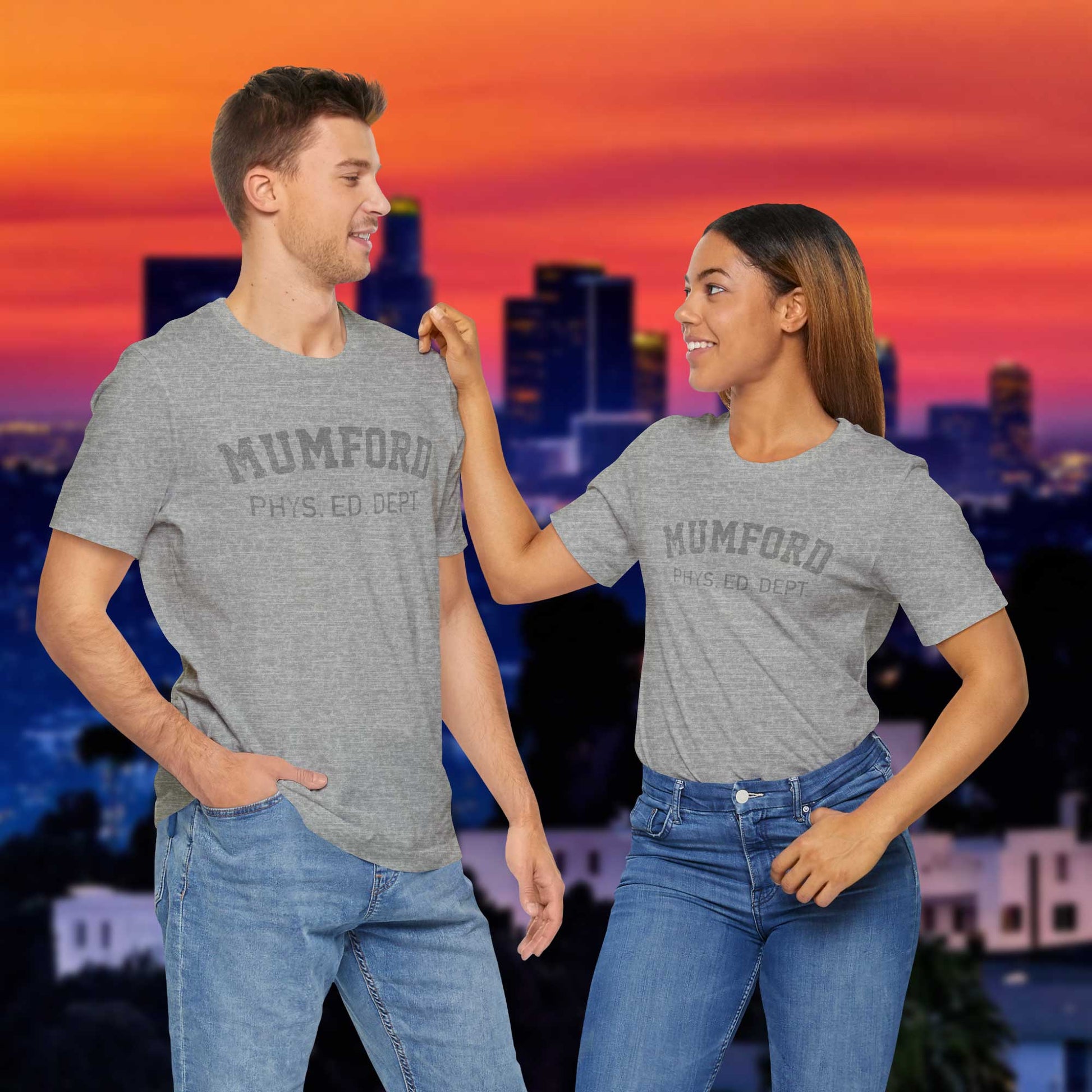 Male and female models wearing Athletic Heather Grey Soft Bella+Canvas 3001 short-sleeve t-shirt gym tees featuring the Mumford Phys Ed logo graphic that Eddie Murphy wore as Axel Foley in the movie Beverly Hills Cop in a vintage distressed style, sold by ScriptedBrand.