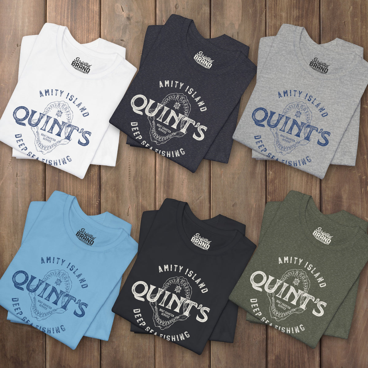 Six folded t-shirts featuring the Quint's Deep Sea Fishing Boat Charters logo graphic inspired by the movie Jaws in a vintage distressed style.