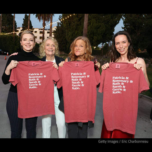 Four women from the show Widow's Bay standing outdoors at an event in LA holding up matching crimson T-shirts printed with the names 'Patricia & Rosemary & Ruth & Sarah & Gerrie & Katie' in white text.