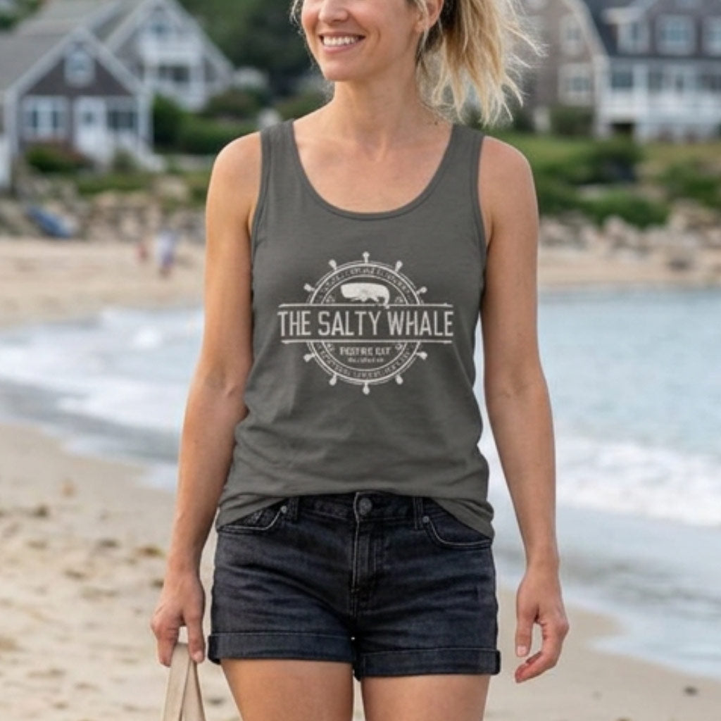 Woman on beach wearing pepper gray garment-dyed tank top with vintage Widow's Bay The Salty Whale nautical crest design