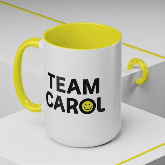 Video of ceramic accent mug with yellow handle and interior, TEAM CAROL text and smiley face from Pluribus